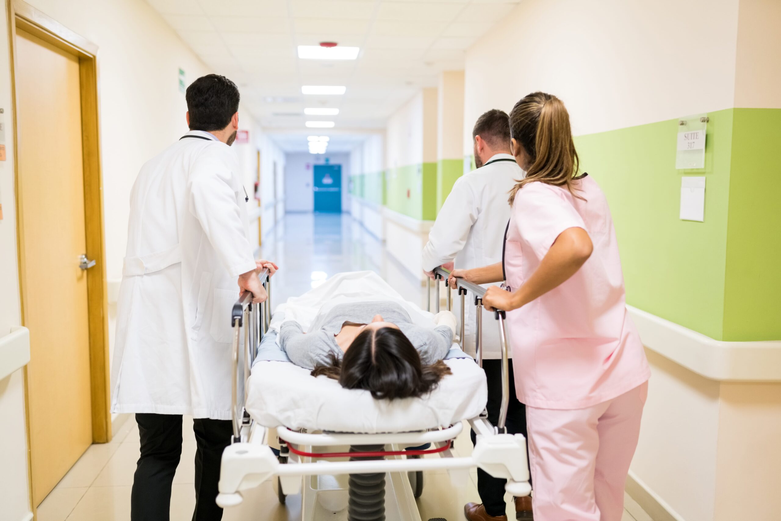 doctors-nurse-pushing-female-patient-stretcher-corridor-hospital-min